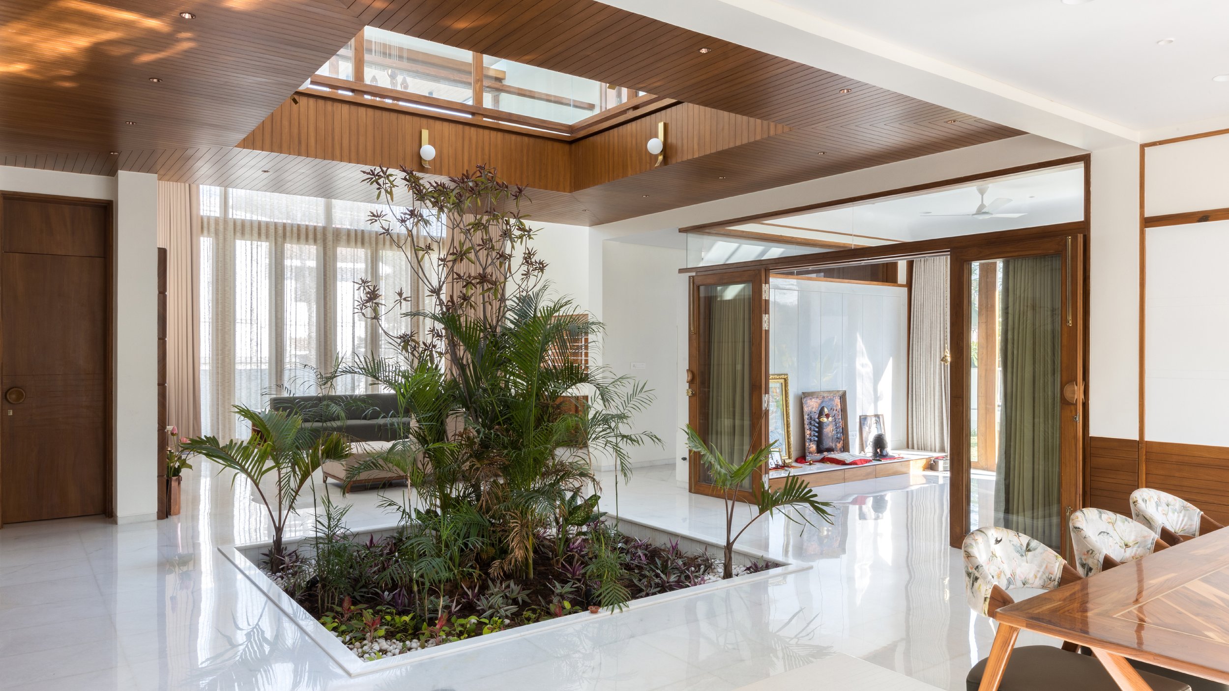 Modern living space with indoor garden, wooden ceiling, and large windows, featuring a dining table and chairs.