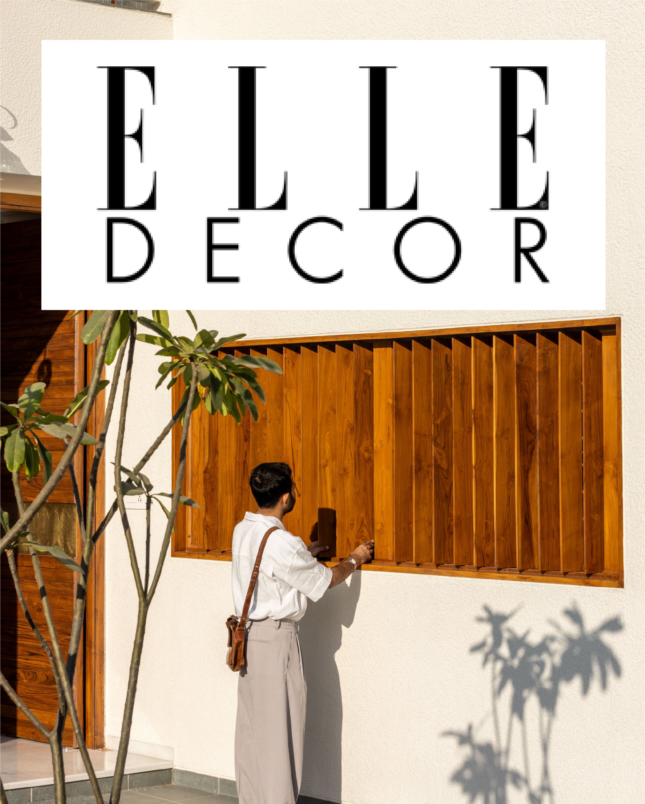 Person standing at a wooden window shutter on a white wall, with a tree casting a shadow. "Elle Decor" logo above.
