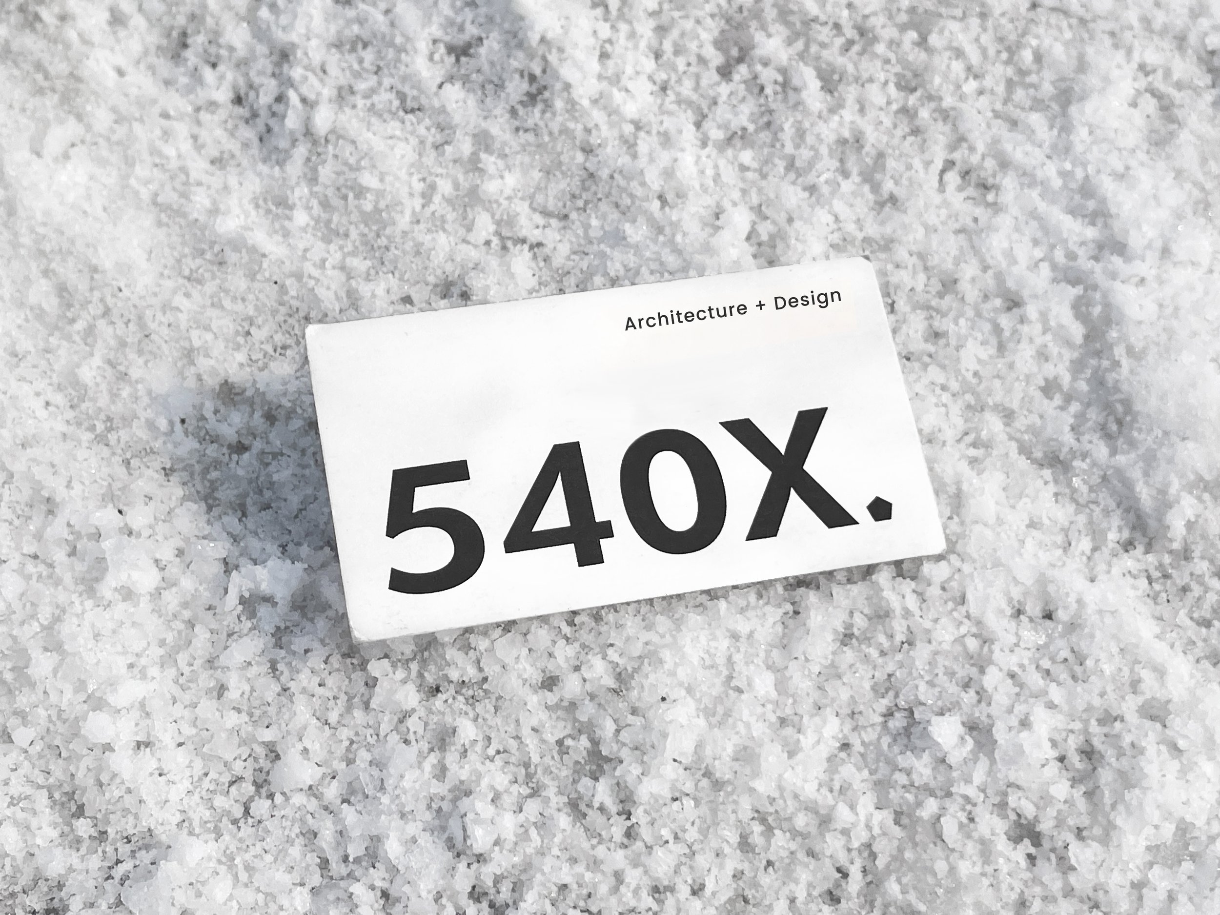 White card reading "Architecture + Design 540X." placed on a snow-covered surface.