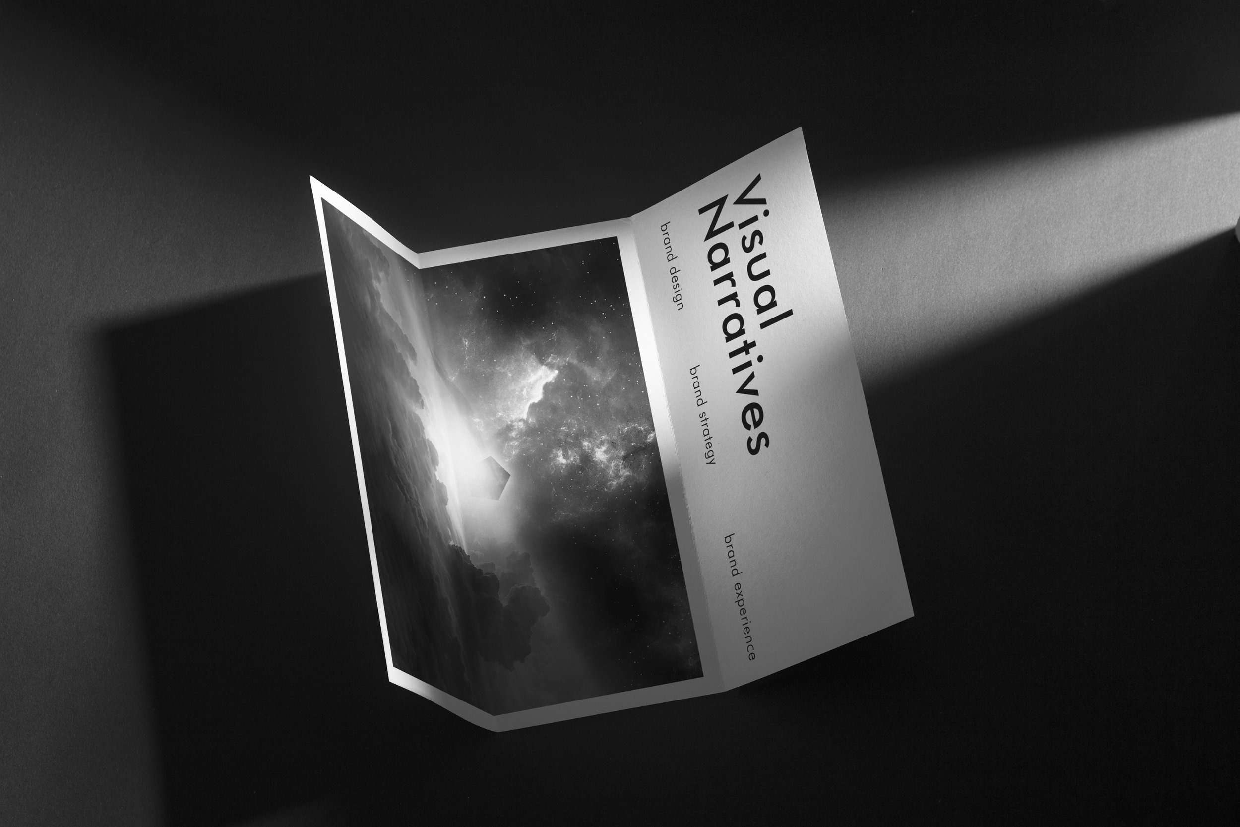 Black and white paper folded, titled "Visual Narratives" with design elements and cosmic imagery, highlighted by a light beam.