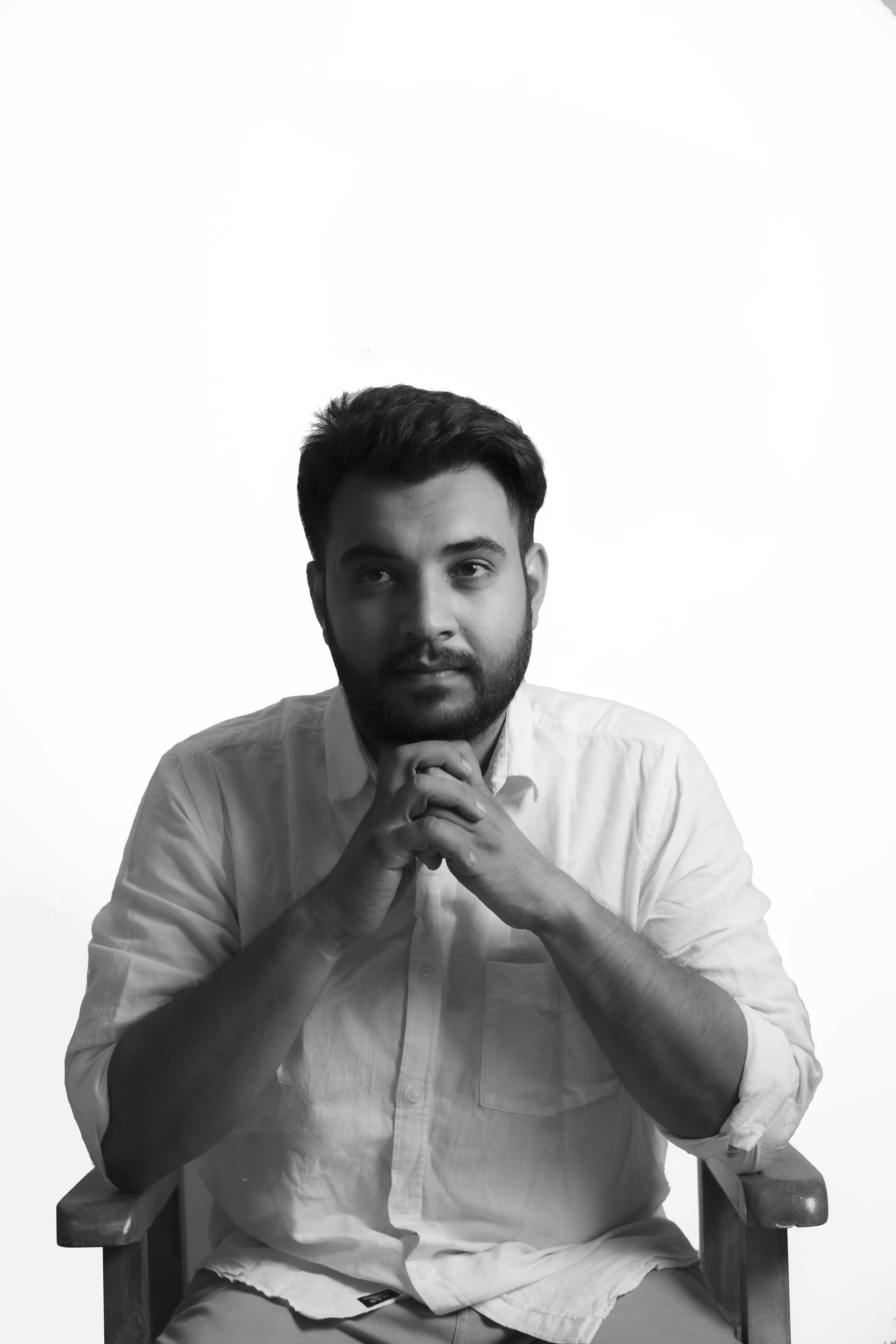Black and white portrait of a man in a white shirt, seated with hands clasped under his chin.